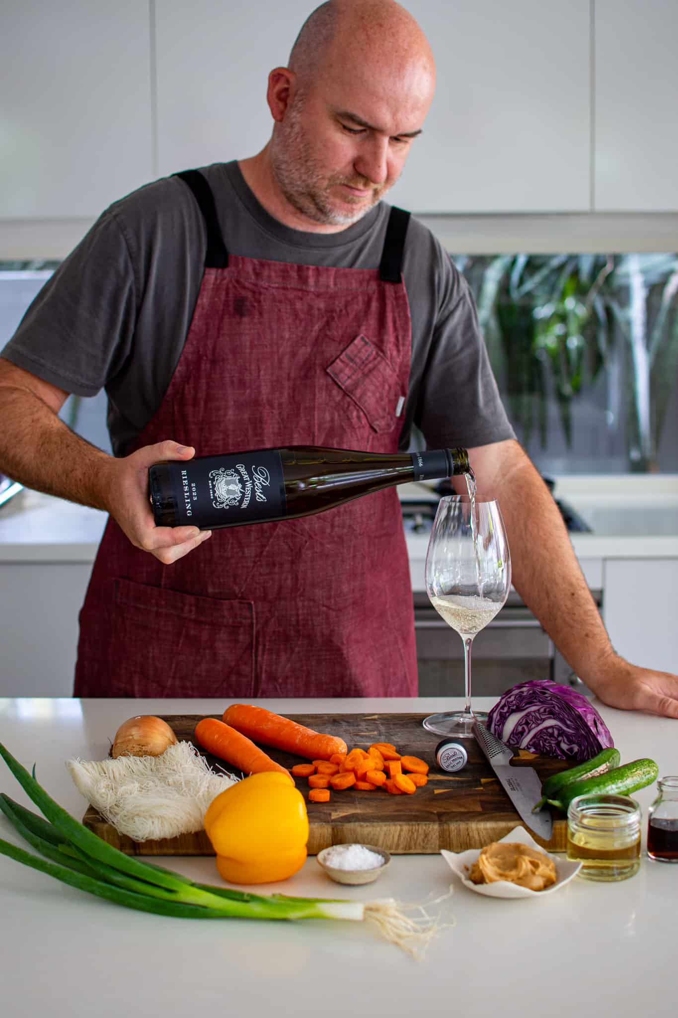 someone in the kitchen pouring a glass of riesling with salad ingredients on the counter