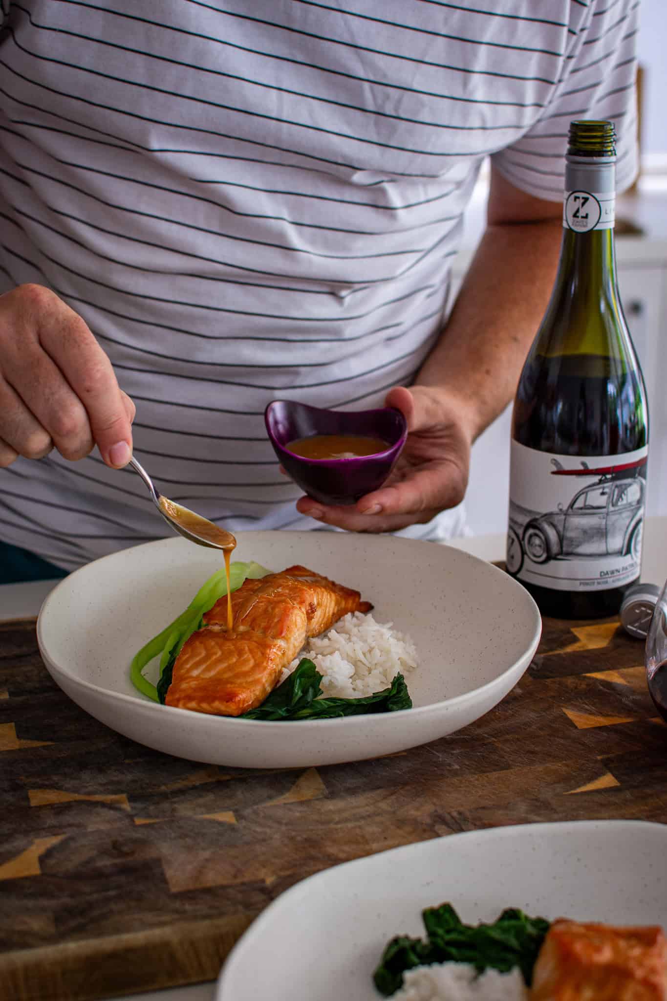 in the kitchen with someone drizzling miso ginger dressing over salmon